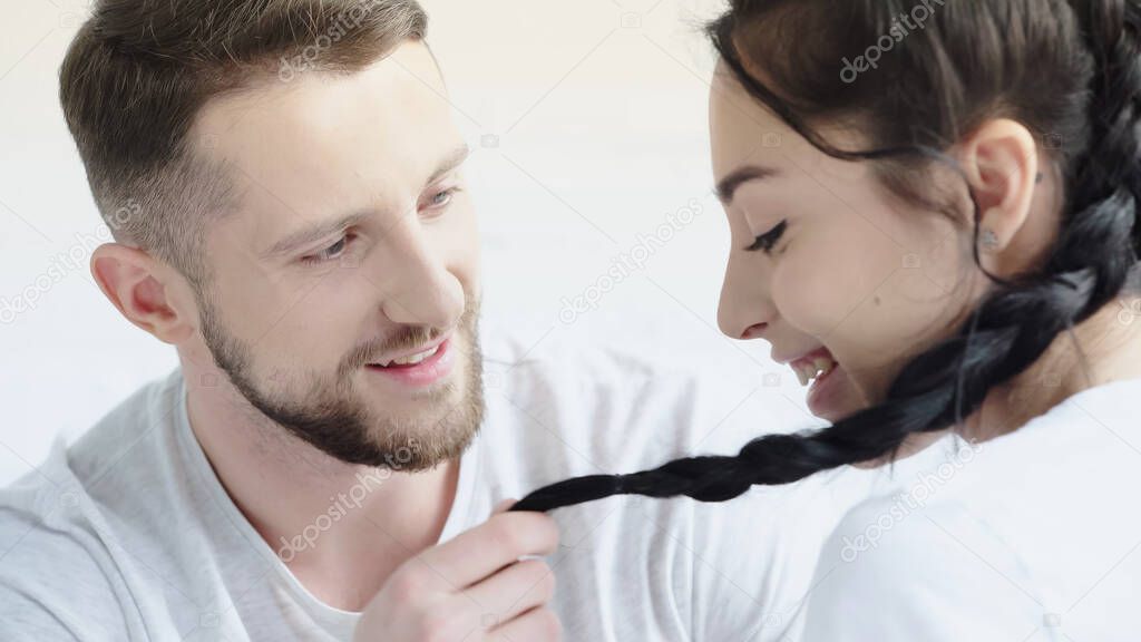 happy man touching braids of smiling girlfriend at home