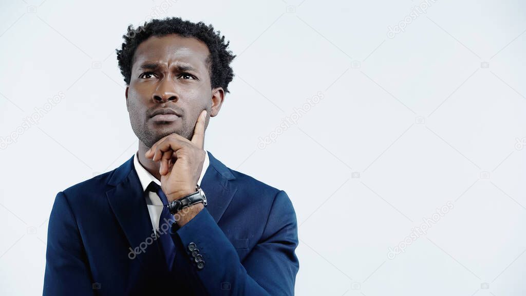 pensive african american businessman in suit looking away while thinking isolated on blue