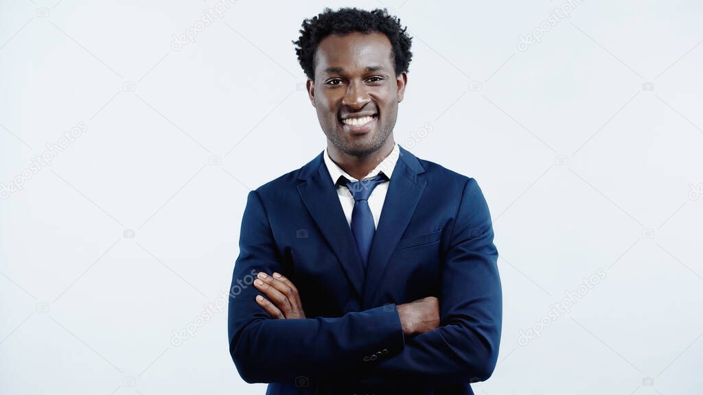 happy african american businessman in formal wear standing with crossed arms isolated on blue