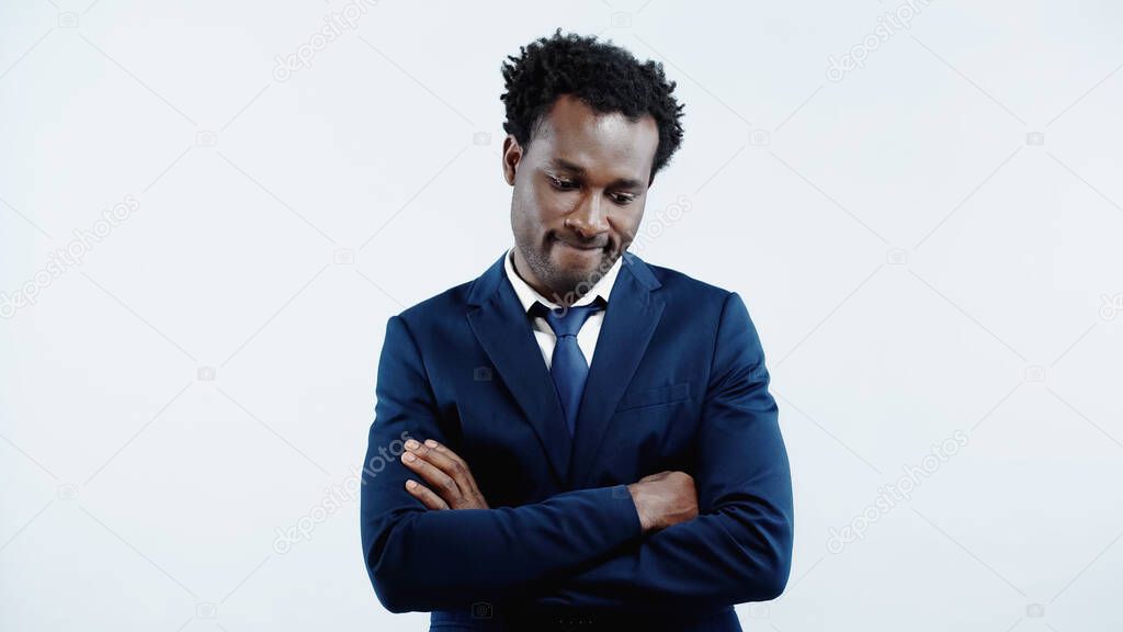 frustrated african american businessman in formal wear standing with crossed arms isolated on blue