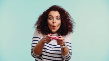 KYIV, UKRAINE - 30 Haziran 2021: Pembe joystick tutan ve mavi üzerinde video oyunu oynayan genç şaşkın kadın