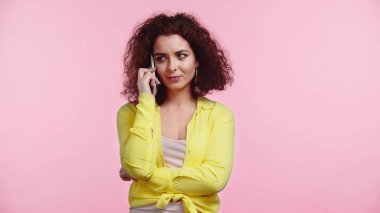 Kıvırcık kadın cep telefonuyla konuşurken pembe renkte izole edilmiş. 