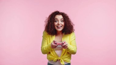 KYIV, UKRAINE - 30 Haziran 2021: Pembe üzerine izole edilmiş, elinde joystick tutan ve dilini dışarı çıkaran pozitif genç kadın 