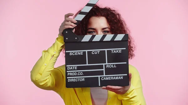 Rizado Joven Mujer Oscureciendo Cara Con Clapboard Aislado Rosa — Foto de Stock