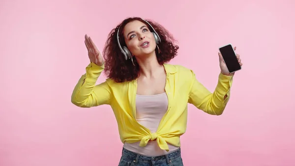 戴无线耳机的年轻女性 手持智能手机 屏幕空白 粉色隔离 — 图库照片