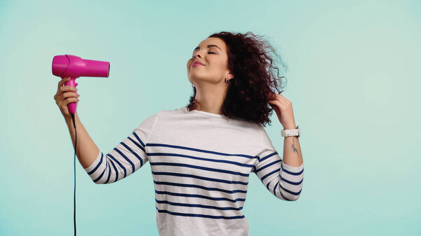 happy young woman drying curly hair isolated on blue 