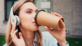 mladá žena v bezdrátových sluchátek pití kávy jít do blízkosti budovy
