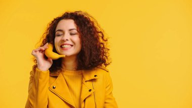 Sarı renkte izole edilmiş muzla telefon konuşması yapan mutlu genç bir kadın.