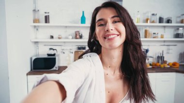 Sütyen ve düğmeleri açık gömlekli neşeli bir kadın bulanık ön planda selfie çekerken kameraya bakıyor.