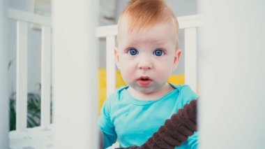 Bulanık bebek beşiğinde yumuşak oyuncağıyla oturan bebek.