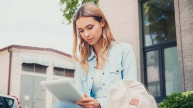 Dışarıdaki binanın yanında dijital tablet kullanan genç bir öğrenci. 