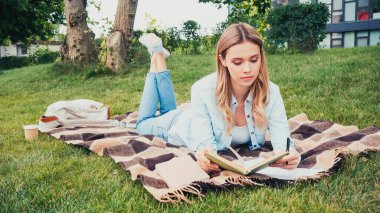 Genç öğrenci parkta defter okuyup yazıyor.