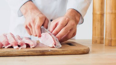 partial view of chef slicing pork tenderloin on chopping board on white clipart