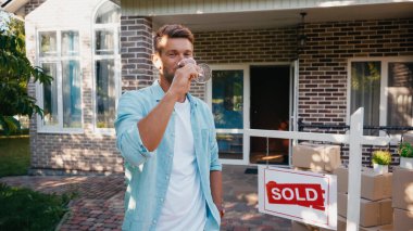 man holding glass and drinking wine near new house  clipart