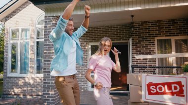 happy man holding keys near wife and dancing near new house and sold board  clipart
