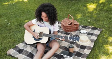 overhead view of happy african american woman playing acoustic guitar during picnic in park  clipart