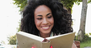 Gülümseyen Afro-Amerikan kadın ciltli kitap okuyor. 