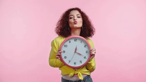 Mujer Joven Rizada Sosteniendo Reloj Pucheros Labios Aislados Rosa —  Fotos de Stock