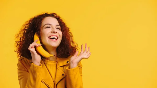 Kręcona Kobieta Naśladująca Rozmowę Telefoniczną Bananem Uśmiechnięta Odizolowana Żółto — Zdjęcie stockowe