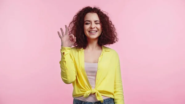 Joyful Young Curly Woman Showing Sign While Winking Isolated Pink — Stock Photo, Image
