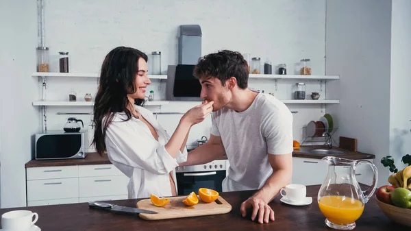 Joyful Woman White Shirt Feeding Boyfriend Juicy Orange Kitchen — Stock Photo, Image