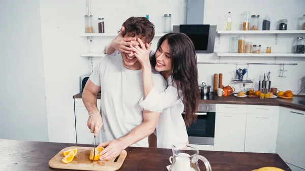 Cheerful Woman White Shirt Covering Eyes Man Cutting Orange Kitchen — Stock Photo, Image