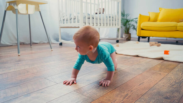 infant boy crawling on floor near feeding chair in living room 