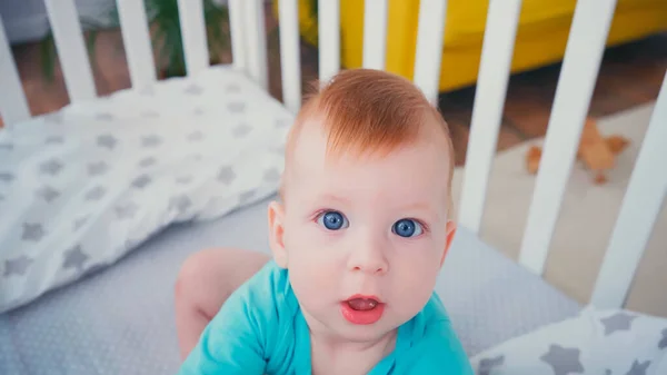 赤ん坊の男の子がカメラを見ているとぼやけたベビーベッドで柔らかいおもちゃで遊んでいるの高い角度のビュー — ストック写真