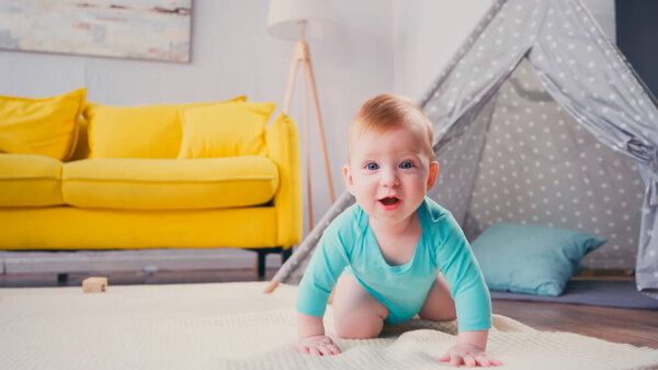happy infant boy crawling on blanket near tipi in living room 