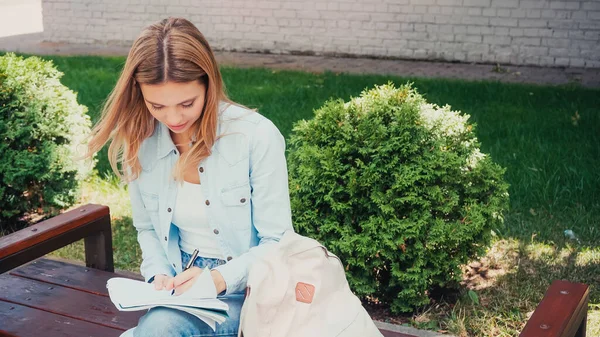 Estudiante Escribiendo Cuaderno Mientras Está Sentado Banco Afuera — Foto de Stock