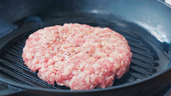 close up of mince patty with salt and black pepper on hot pan