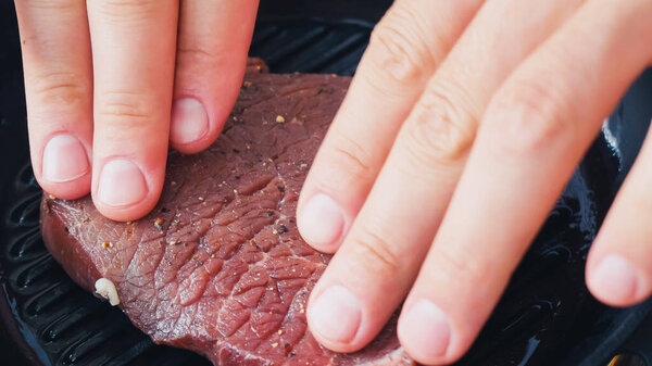 Cropped view of chef putting spiced beef steak on grill pan