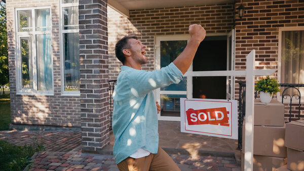 excited man rejoicing near sold board and new house