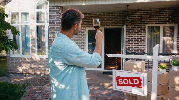 man holding glass of wine and looking at new house 