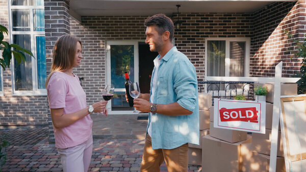 side view of happy man holding bottle with red wine near wife and new house 