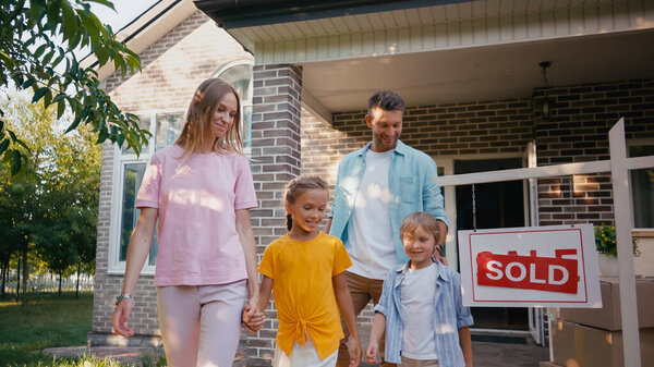 mother holding hands with daughter while walking with son and husband near new house 