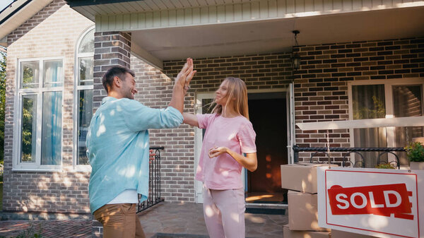 happy couple giving high five near new house and sold board 