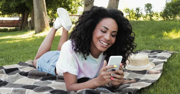 Pleased African American Woman Using Smartphone While Lying Checkered Blanket — Stock Photo, Image