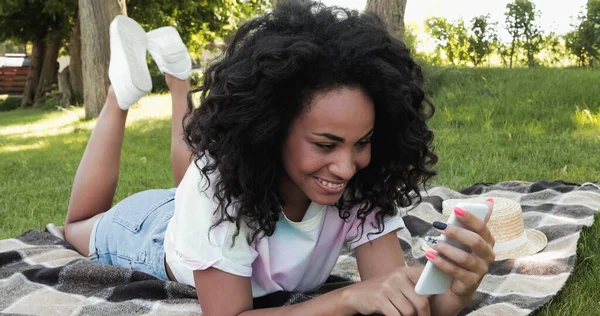 Alegre Mujer Afroamericana Usando Teléfono Inteligente Mientras Está Acostado Manta — Foto de Stock