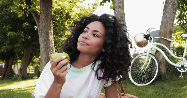 Mujer Afroamericana Rizada Comiendo Manzana Fresca Cerca Bicicleta Parque — Foto de Stock