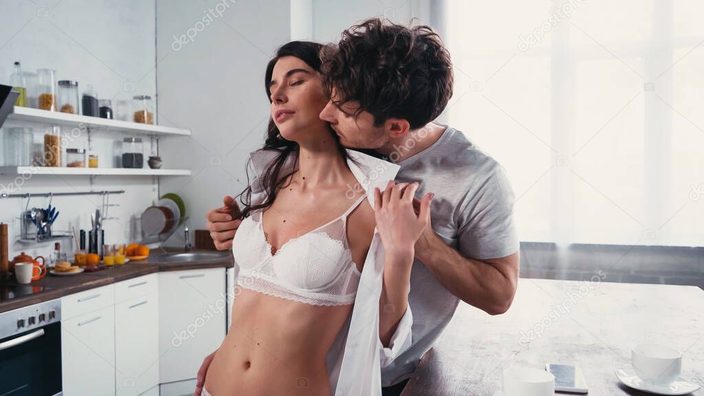 young man taking off shirt from sexy woman in white bra in kitchen
