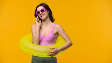 Mayo giymiş ve güneş gözlüklü bir kadın sarıda izole bir şekilde akıllı telefondan konuşuyor.