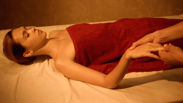 young client with closed eyes receiving hand massage from masseur in spa salon