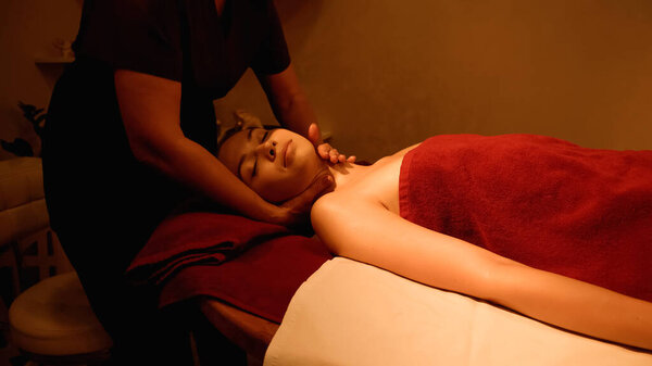 young woman with closed eyes receiving neck massage from masseur in spa salon