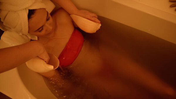 high angle view of professional therapist doing massage with sea shells to young client in bathtub