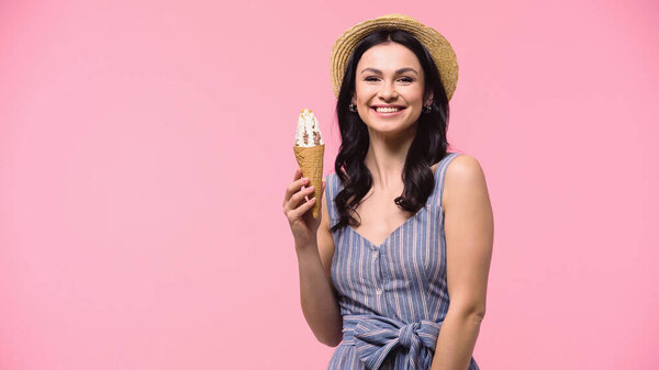 Smiling woman in straw hat holding ice cream isolated on pink 
