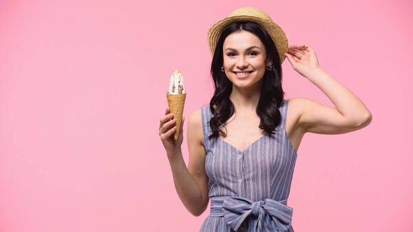 Cheerful woman in sun hat holding ice cream and looking at camera isolated on pink 