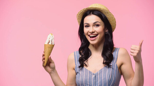 Excited woman in sun hat showing like while holding ice cream isolated on pink 