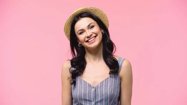 Hasır şapkalı esmer kadın kameraya bakıyor ve pembe üzerine izole bir şekilde gülümsüyor. 