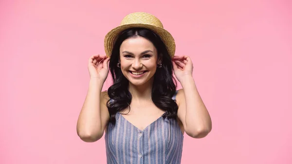 Mujer Bonita Sonriendo Cámara Mientras Sostiene Sombrero Sol Aislado Rosa — Foto de Stock